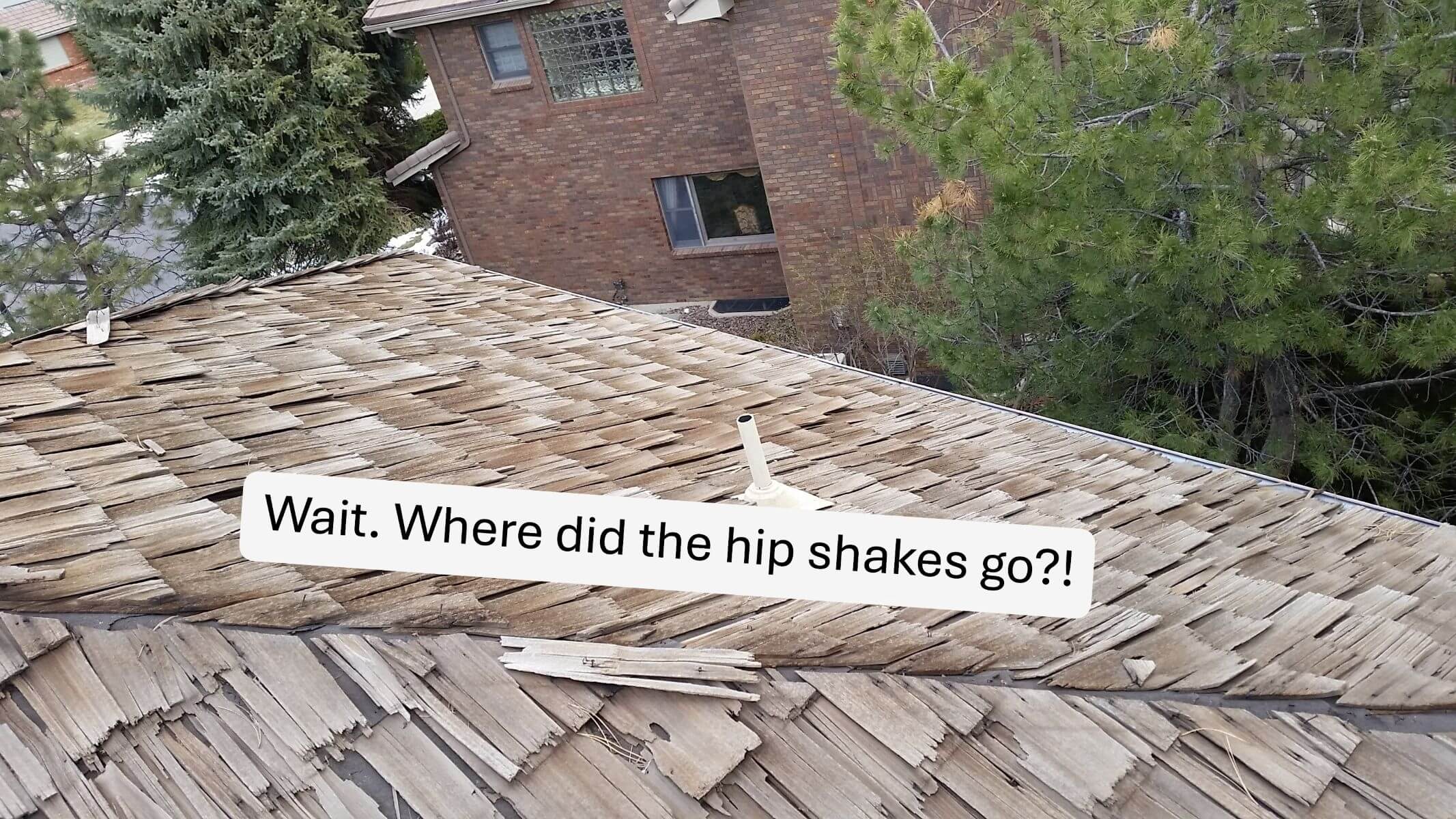 A wood shake roof with an entire section of hip shingles blown off by wind.