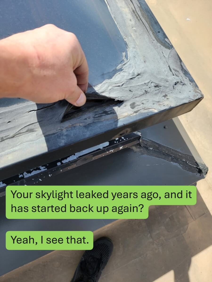 A hand peeling back failed sealant tape on a commercial skylight.